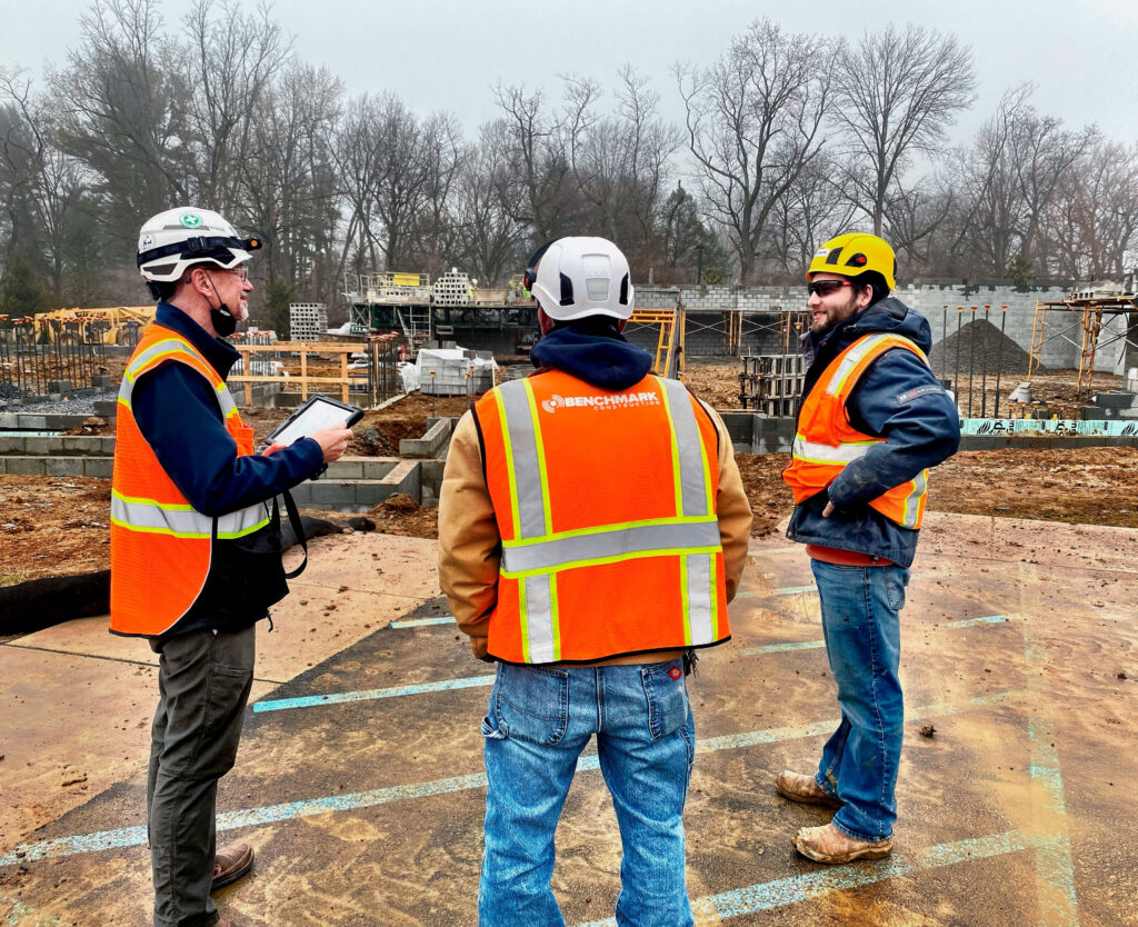 Three Benchmark employees at a job site reviewing plans on a tablet