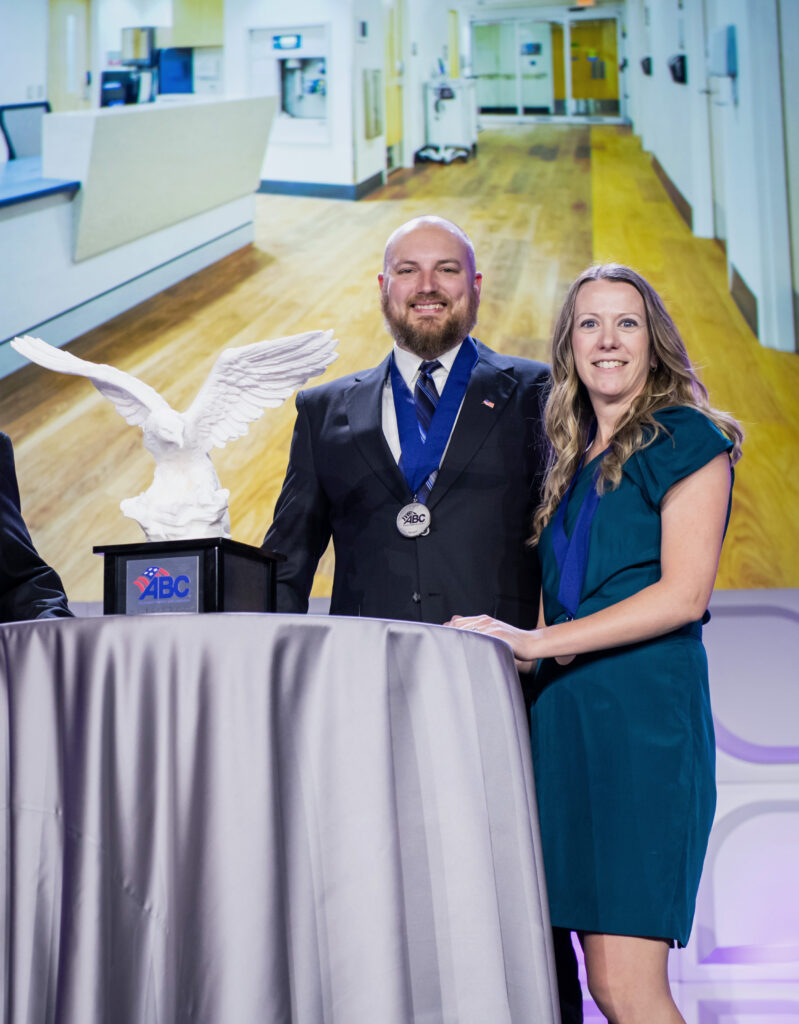 Two people smiling for the camera while they accept an award and both wear medals