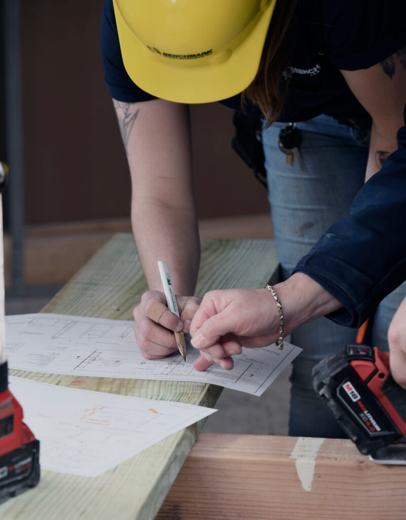 Overhead view of two Benchmark employees making adjustments to blueprints