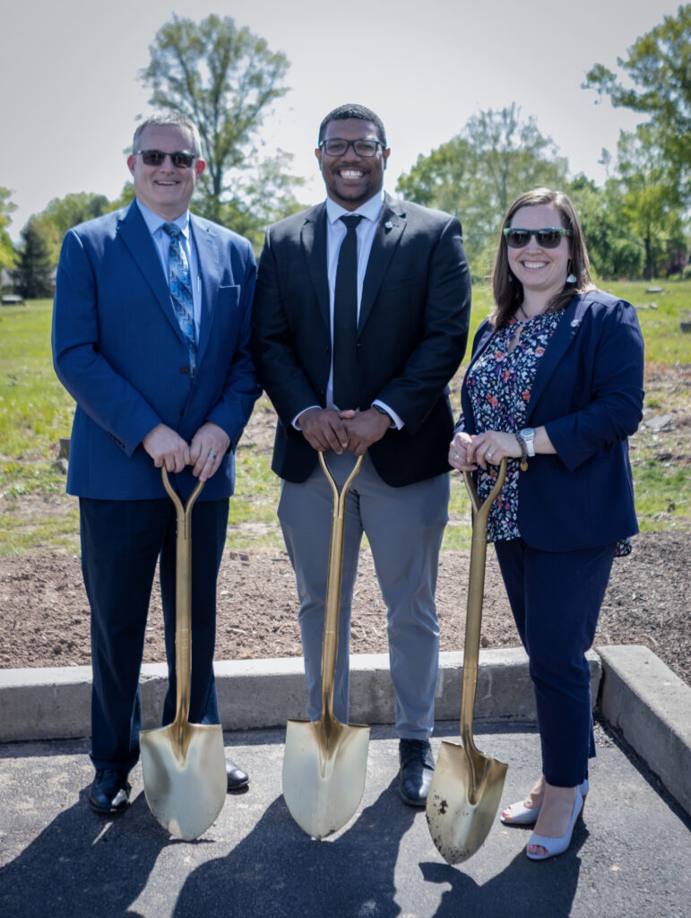 Three Benchmark team members each holding a golden shovel and smiling