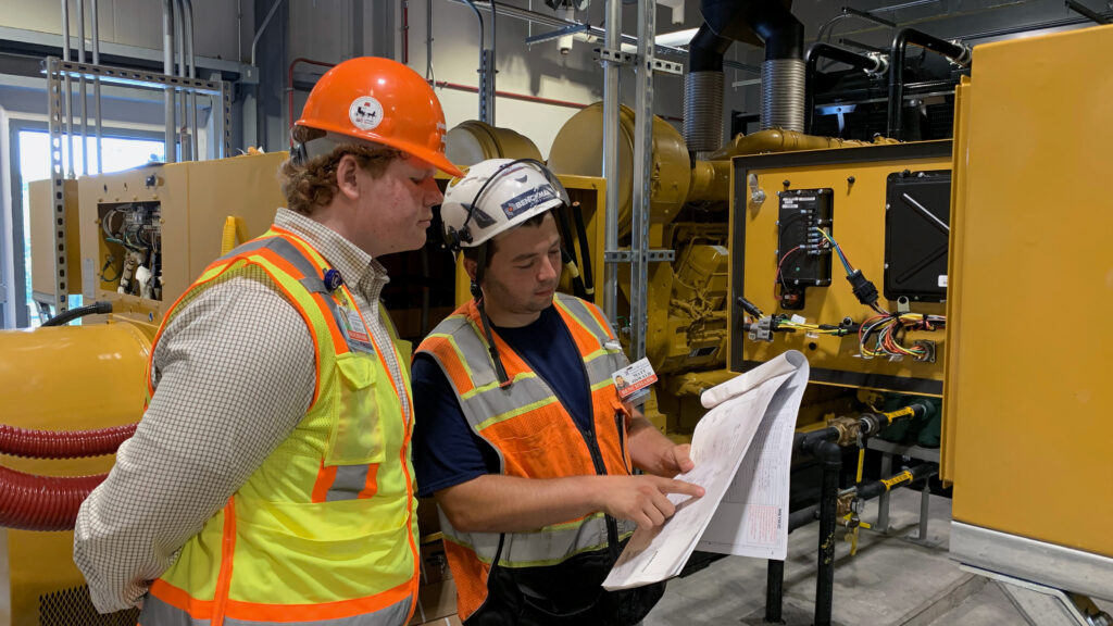 Two Benchmark team members dressed in safety gear reviewing a blueprint on a job site 