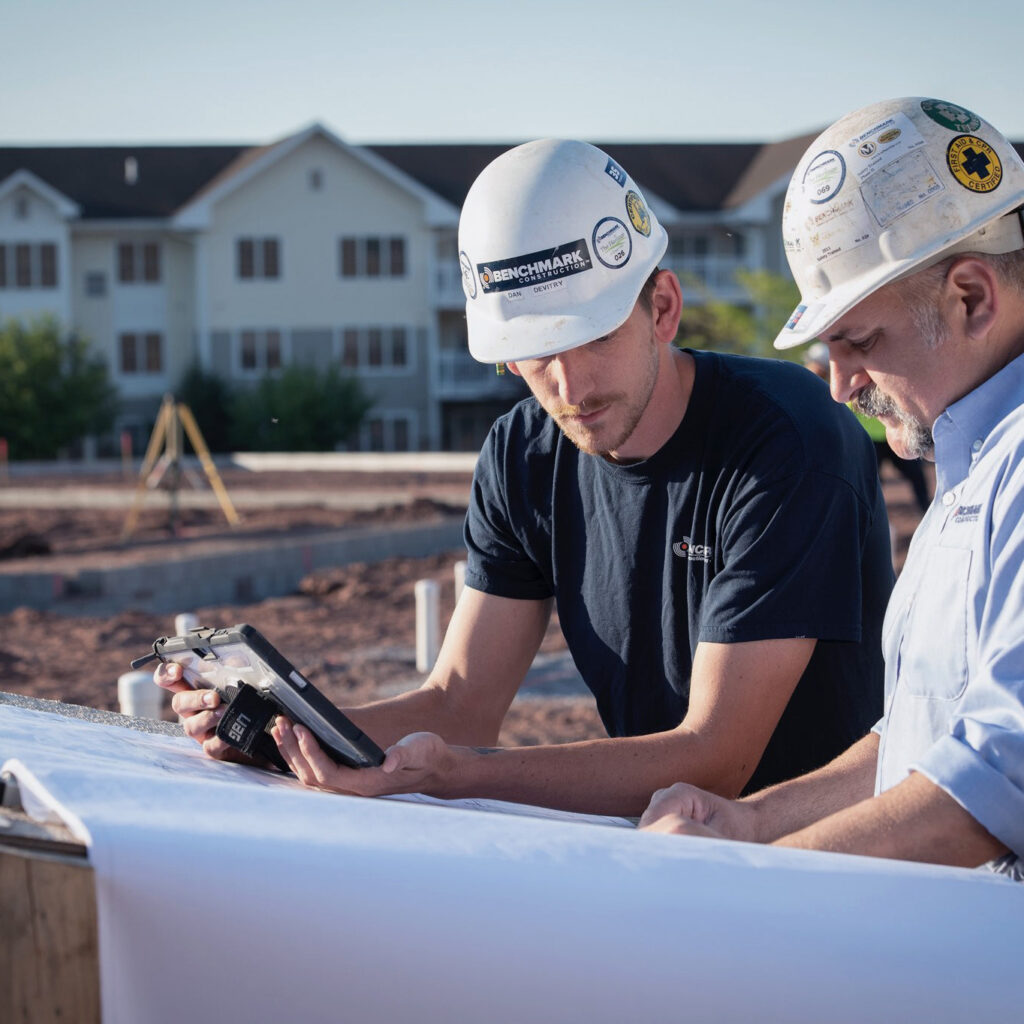 Two Benchmark employees at an outdoor general contracting job site reviewing plans