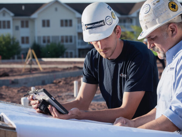 Two Benchmark employees at an outdoor general contracting job site reviewing plans