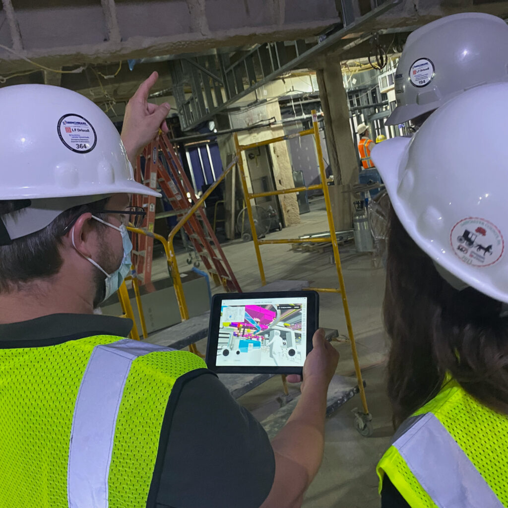 Over the shoulder view of three Benchmark employees reviewing digital plans on a tablet at a job site