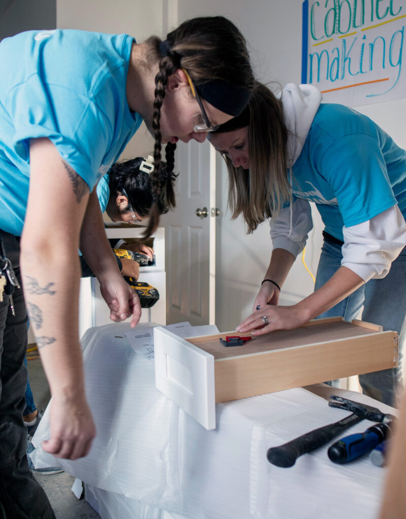 Three people working together to put together cabinets